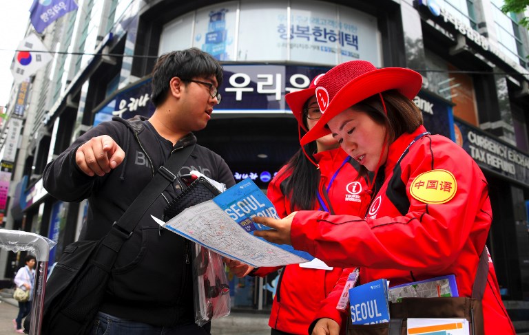 South Korean tourist information helpers (red) guide tourists in the popular Myeongdong shopping district in Seoul on April 25, 2017. South Korea's tourist industry has been hammered by China's boycott over the deployment of US missile defence system, with visitor numbers from the Asian giant plummeting 40 percent in March, statistics showed. / AFP PHOTO / JUNG Yeon-Je