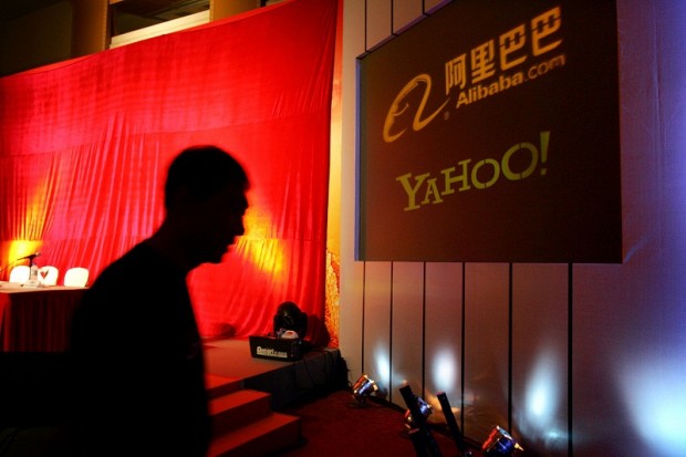 In this Aug. 11, 2005, file photo, a man walks past a screen displaying the Yahoo and Alibaba.com logos before a joint news conference by the companies at the China World hotel in Beijing. Yahoo announced that it has agreed to sell half of its 40 percent stake in Chinese e-commerce company Alibaba for about $7.1 billion. The deal will see Alibaba Group buying back the stake from Yahoo Inc. for $6.3 billion cash and up to $800 million of Alibaba preference shares.  AP PHOTO