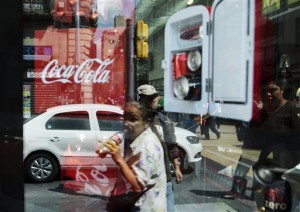 A woman is reflected in a Coca-Cola store window display as she drinks a Coke in Mexico City, Thursday, Oct. 9, 2014.  AP