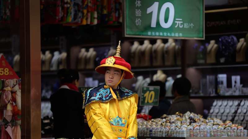 In this Oct. 21, 2014 file photo, a worker dressed an emperor costume to attract customers as he stands outside a shop selling souvenirs at the Wangfujing shopping district in Beijing, China. An Associated Press survey of 30 economists has found that 57 percent of them expect China’s decelerating economy to restrain growth in countries from Brazil and Chile to Australia and South Korea. A notable exception is the United States, which the economists see as largely insulated from China’s troubles. (AP Photo/Andy Wong, File)