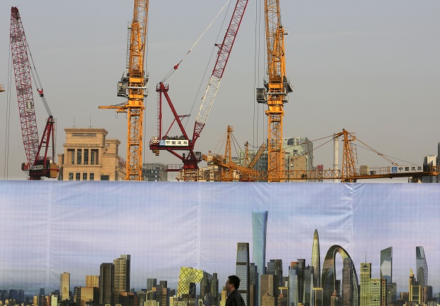 FILE - In this Tuesday, Oct. 21, 2014 file photo, a man walks past a billboard displaying the future skyline, near a construction site in Beijing, China. For the Chinese economy, the worlds second-largest,  its been a year of flux. Though its slowdown may not be dramatic, it is one of the global economic concerns going into 2015. (AP Photo/Andy Wong, File)