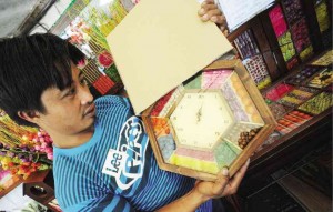 JUANITO Baterzal of Benelco Arts & Crafts holds a wall clock with colorful dried botanical seeds and foliage. 