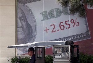 A man waits for customers while sitting on his tricycle in front of a hundred US dollar banknote poster outside a bank in Beijing, China, Wednesday, May 12, 2015. Asian stock markets were mostly higher Wednesday, overcoming initial caution after a bond sell-off nudged Wall Street lower.  AP PHOTO/ANDY WONG