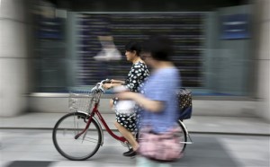 A woman rides a bicycle past an electronic stock board of a securities firm in Tokyo Tuesday, May 26, 2015. Major Asian markets mostly rose Tuesday, with Hong Kong and Shanghai leading the way, while Tokyo marked an eighth straight gain to a 15-year high.  AP PHOTO/EUGENE HOSHIKO