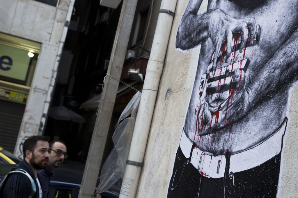 Pedestrians look at a mural, partially seen, with hands squeezing a bleeding Euro sign in Athens, on Saturday, June 27, 2015. Greece's place in the euro currency bloc looked increasingly shaky on Saturday after eurozone nations rejected a month-long extension to its bailout program and the prime minister called for a risky popular vote on the country's financial future.(AP Photo/Petros Giannakouris)