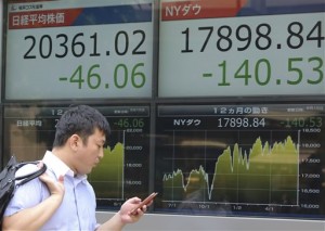 A man checking his mobile phone walks by an electronic stock board of a securities firm in Tokyo Monday, June 15, 2015. Asian markets mostly headed lower Thursday, June 18, and the dollar retreated after the Federal Reserve said any rises in US interest rates would be slow.  AP PHOTO/KOJI SASAHARA