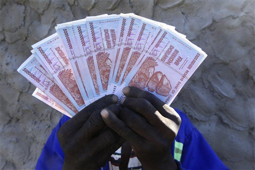 A man holds a handful of 5 Billion Zimbabwean dollar notes, in Harare, Friday, June, 12, 2015. AP