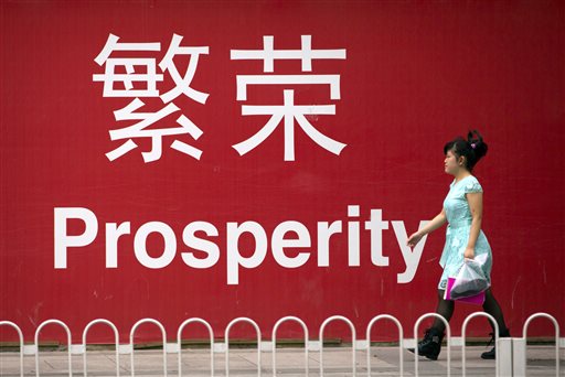 In this July 15, 2015 photo, a woman walks past a sign reading "Prosperity" in Chinese and English in Beijing. China's economic growth decelerated in the latest quarter but relatively robust spending by Chinese consumers helped to avert a deeper downturn. The world's second-largest economy grew by 6.9 percent in the three months ended in September, the slowest since early 2009 in the aftermath of the global crisis, data showed Monday, Oct. 19, 2015. That was down from the previous quarter's 7 percent. (AP Photo/Mark Schiefelbein)