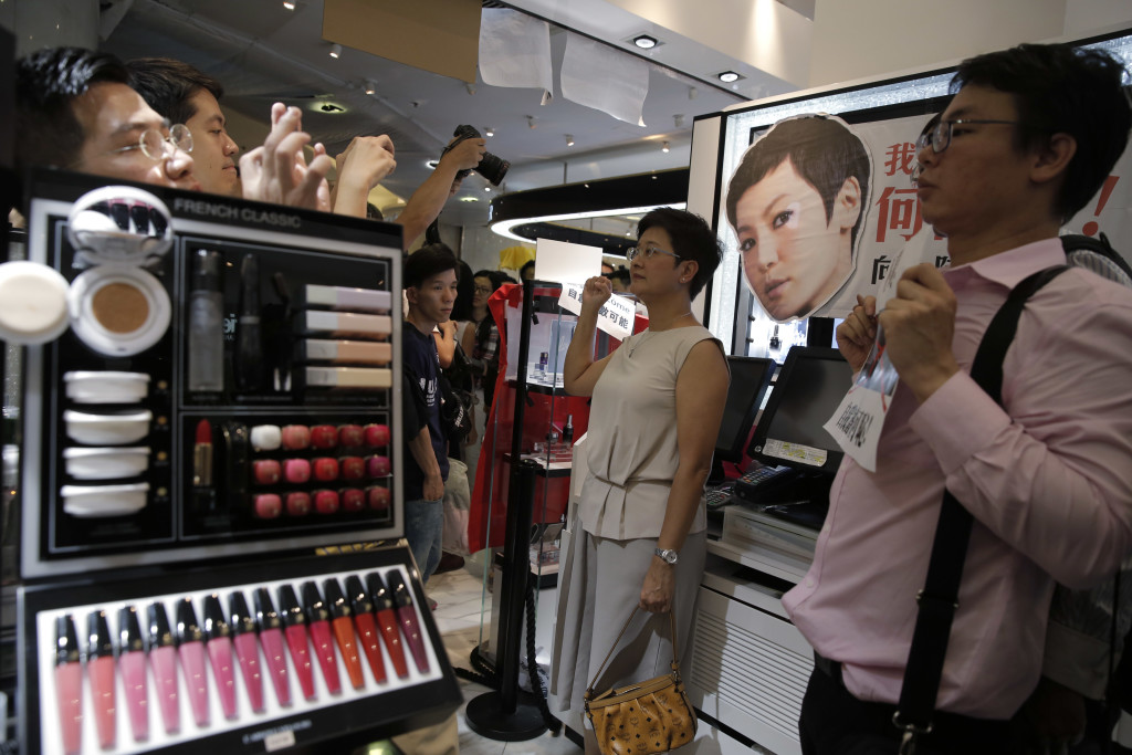 Protestors display placards and the picture of local singer Denise Ho at a Lancome counter inside a department store at Hong Kong's Times Square, Wednesday, June 8, 2016. French cosmetics company Lancome has sparked a backlash in Hong Kong after it canceled a promotional concert featuring a singer known for pro-democracy views, with many accusing it of caving to political pressure from Beijing. (AP Photo/Kin Cheung)