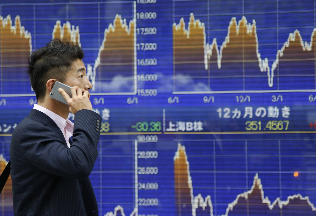 A man speaks on a smartphone in front of the electronic stock indicator of a securities firm in Tokyo, Thursday, June 9, 2016. Asian shares were mostly lower Thursday despite gains on Wall Street as a weaker dollar negatively impacted Japanese stocks and investors weighed risks given the Federal Reserve's cautious stance about tightening rates. (AP Photo/Shizuo Kambayashi)