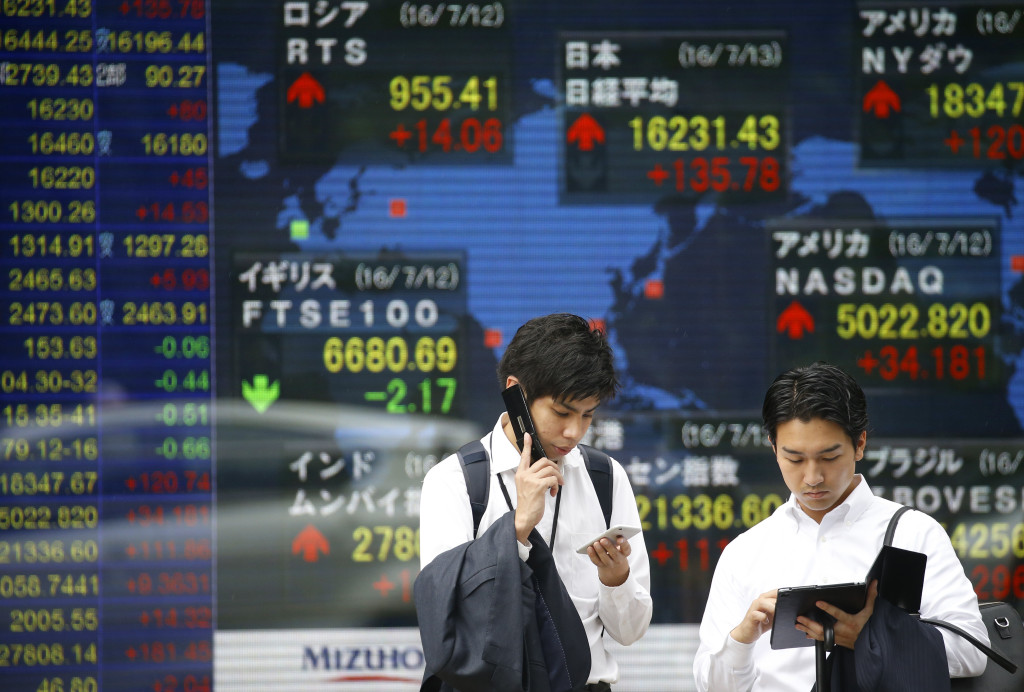 A man uses a mobile phone in front of an electronic stock indicator of a securities firm in Tokyo, Wednesday, July 13, 2016. Asian stock markets traded higher on Wednesday following Dow's record-high close overnight, as the confirmation of Britain's new leader eased uncertainties while the stimulus hopes also helped lift stocks in the region. (AP Photo/Shizuo Kambayashi)