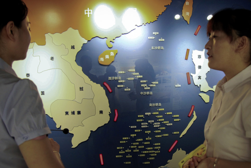 In this Tuesday, July 12, 2016 photo, workers chat near a map of South China Sea on display at a maritime defense educational facility in Nanjing in east China's Jiangsu province. China blamed the Philippines for stirring up trouble and issued a policy paper Wednesday calling the islands in the South China Sea its "inherent territory," a day after an international tribunal said China had no legal basis for its expansive claims. (Chinatopix via AP)