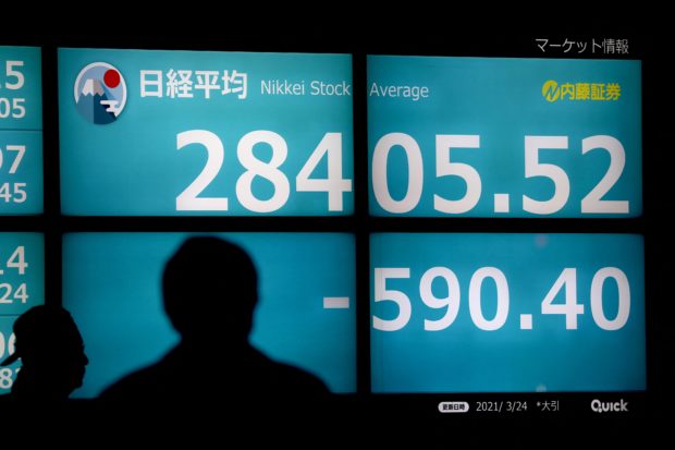 Pedestrians walk past a stock indicator displaying closing numbers of Nikkei 225 of the Tokyo Stock Exchange in Tokyo on March 24, 2021. (Photo by Behrouz MEHRI / AFP)