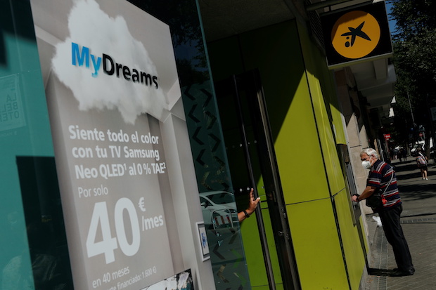 A man uses an ATM machine next to a poster advertising Caixabank's consumer financing programme "MyDreams" in Madrid