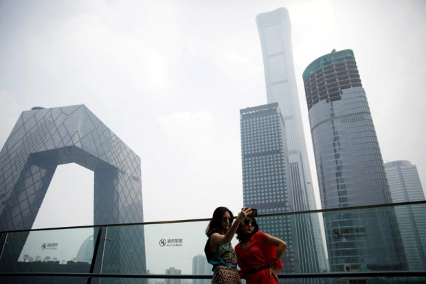 FILE PHOTO: Women pose for pictures at a shopping mall near the CCTV headquarters and China Zun skyscraper in Beijing's central business district (CBD), China, July 16, 2020. REUTERS/Tingshu Wang