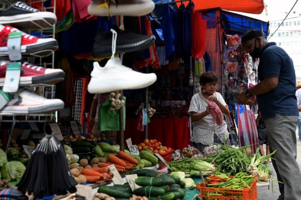 A man buys a vegetables from a street stall in Quiapo, Manila on July 5, 2022. (Photo by JAM STA ROSA / AFP)