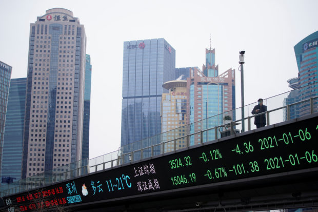 Man standing on an overpass with an electronic board showing stock indices