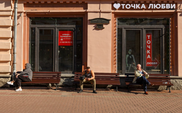 People rest on benches in front of a commercial buildingin Moscow