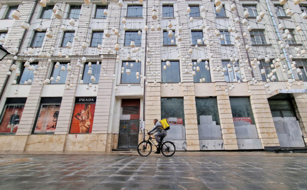 A food courier in bicycle rides past the temporarily closed Prada shop in Moscow
