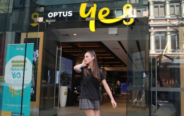 Woman using her mobile phone as she passes the entrance of an Optus shop 