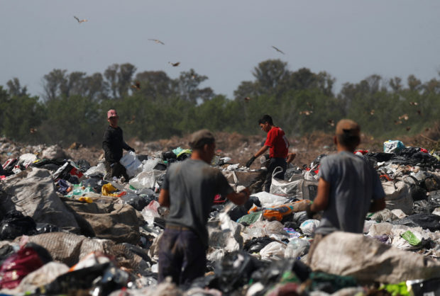 Waste recyclers look through heaps of waste at a landfill for cardboard, plastic and metal,