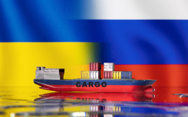 A cargo ship boat model in front of Ukraine's and Russian's flags 