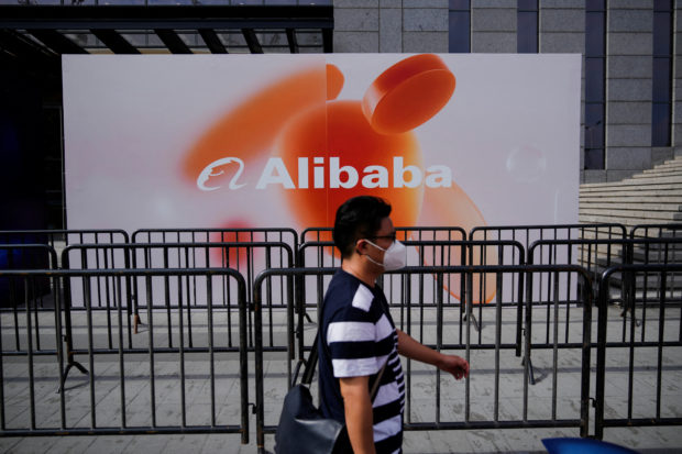 Man walks past a sign of Alibaba Group
