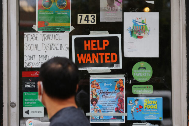 A pedestrian passes a 'help wanted' sign on a door of a hardware store in Cambridge