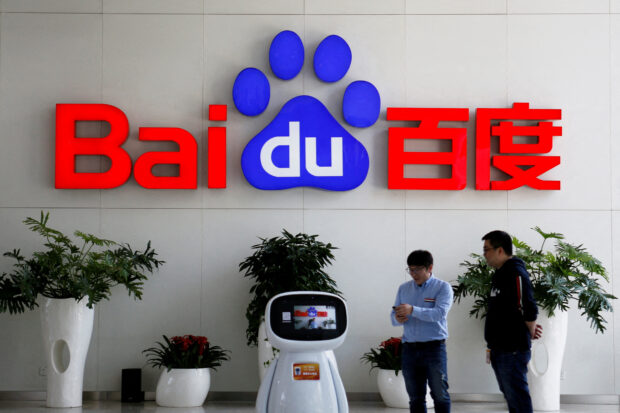 Men interact with a Baidu AI robot near the company logo
