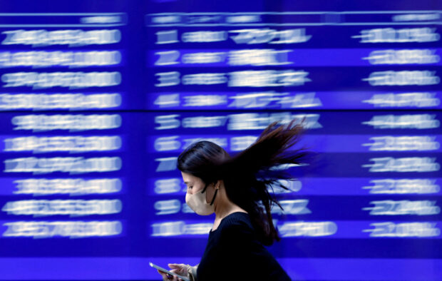 A passerby walks by an electronic monitor displaying stock prices in Tokyo