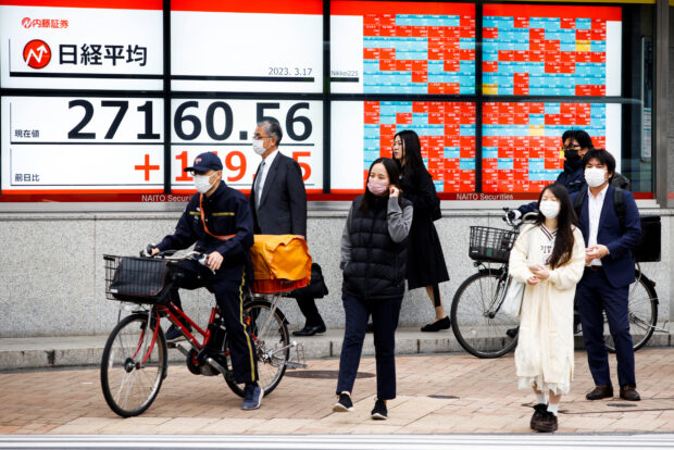 People pass by an electronic board showing the Nikkei average in Tokyo