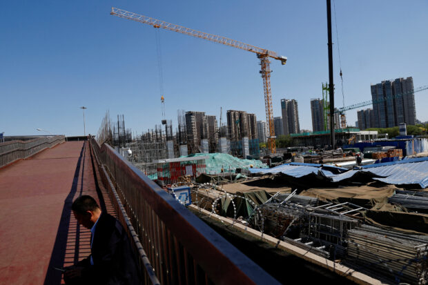 A man sits on an overpass near a construction site of a subway station in Beijing