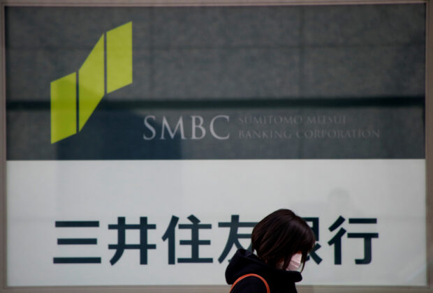 Woman walks past a sign of Sumitomo Banking Corp