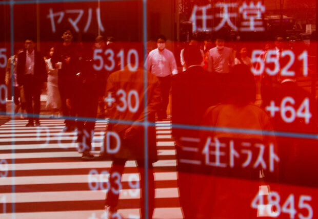 Passersby are reflected on an electronic stocks quotation board in Tokyo