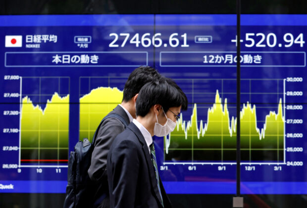 Passersby walk past an electronic stocks monitor inTokyo