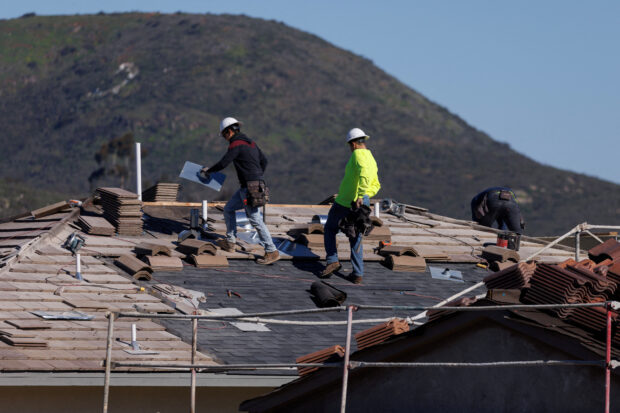 Workers tile a roof on a house under construction in San Marcos, California
