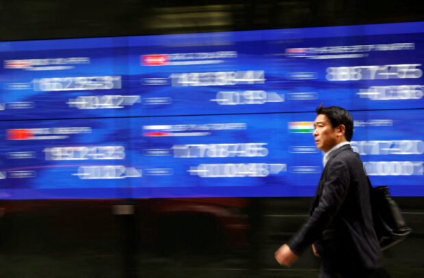 Passerby walks past an electric monitor showing stock prices outside a bank in Tokyo