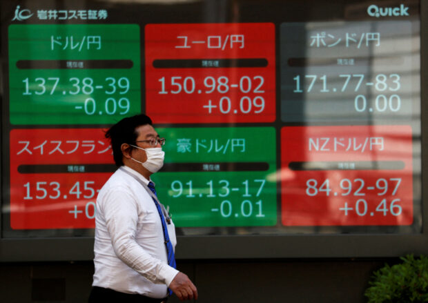 Man walks past an electronic monitor displaying foreign exchange rates in Tokyo