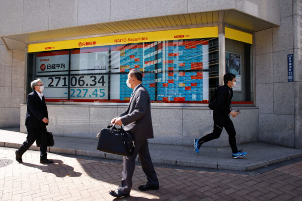 People walk past an electronic board showing Japan's Nikkei average and stock quotations