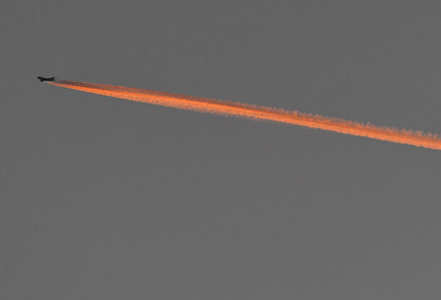 Setting sun illuminates an aircraft's contrail as it flies