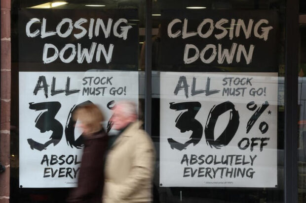 People walk past a shop with closing down signs in Chester, Britain