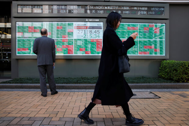 A woman walks past a man checking an electronic board showing Nikkei average and stock quotations