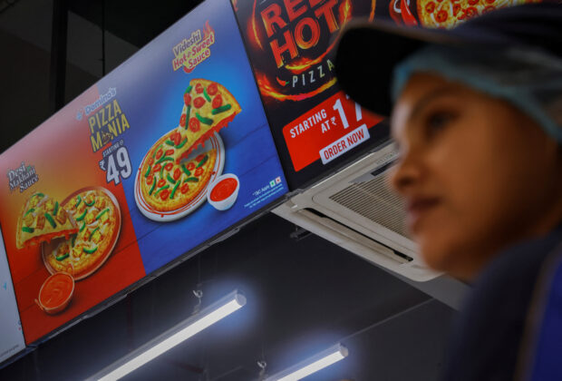 A Domino staff member stands next to a sign for a 49-rupee pizza
