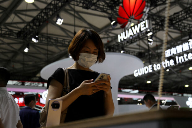 A visitor checks a mobile phone near a Huawei logo 