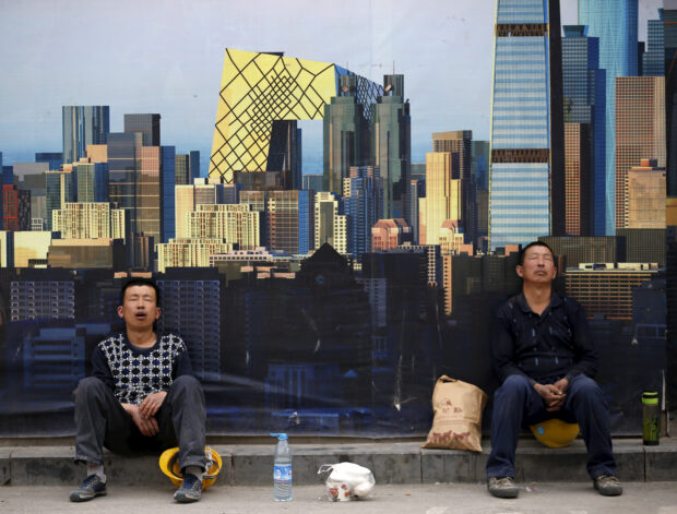Construction workers take a nap in front of a wall of a construction site in Beijing