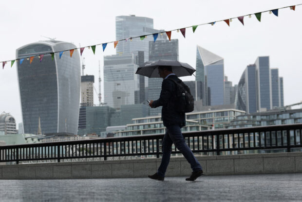 A man walks along the River Thames in view of the City of London skyline