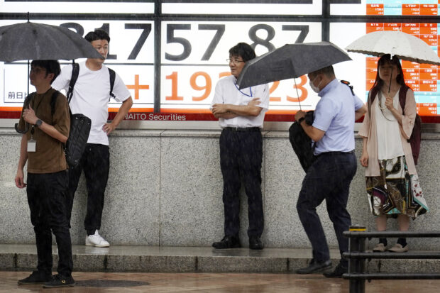 People stand in the rain in front of an electronic stock board in Tokyo