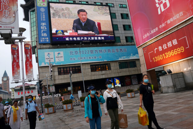 People walk under a giant screen showing a news footage in Beijing