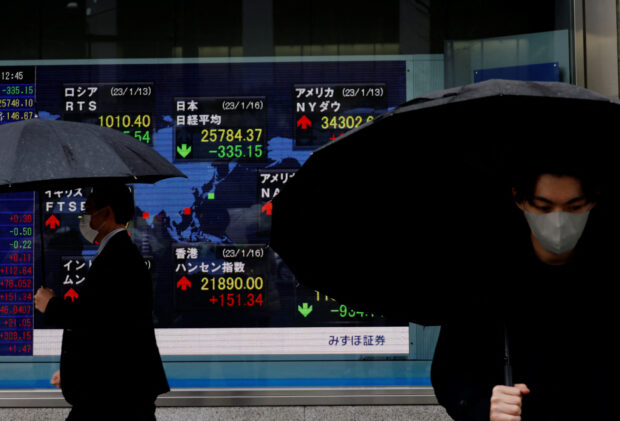 Men walk past an electronic board showing Nikkei and other countries' indexes in Tokyo