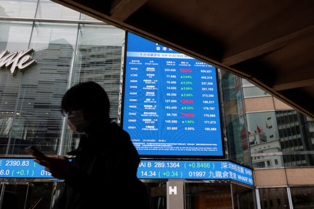 A person walks past a screen displaying the Hang Seng Index in Hong Kong